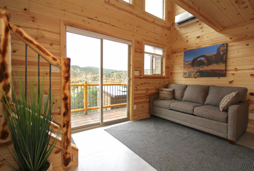 Cozy wooden interior with a gray sofa, large windows, and a view of nature outside.