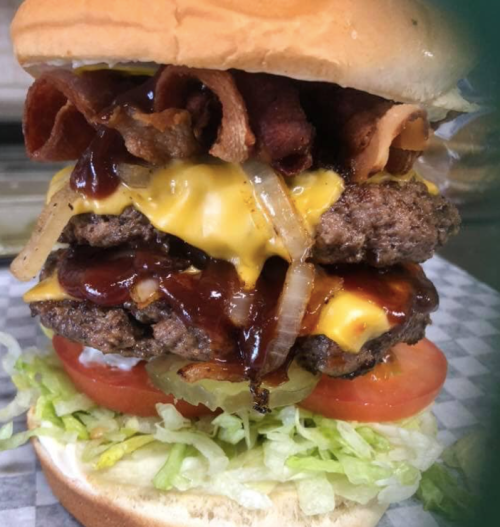 A towering burger with two beef patties, melted cheese, bacon, onions, lettuce, and tomato, all in a soft bun.