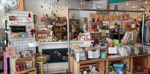 A colorful shop interior filled with various crafts, gifts, and decor items, featuring a cheerful "Happy Up" sign.