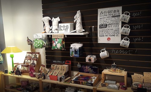 A display of various colorful gifts and decor items on shelves, including bags, stationery, and a lamp.