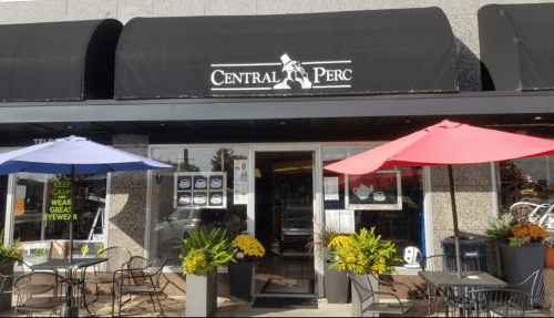 Exterior of Central Perc café with a black awning, colorful umbrellas, and outdoor seating. Flowers decorate the entrance.