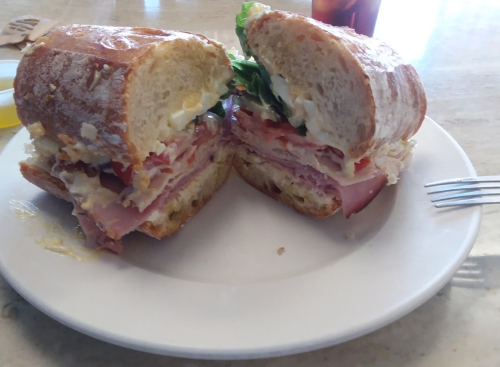 A sandwich with layers of ham, turkey, lettuce, and mayonnaise, served on a toasted roll, on a white plate.