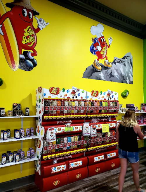 A colorful candy store display featuring Jelly Belly products and a vibrant mural of a character on a yellow wall.