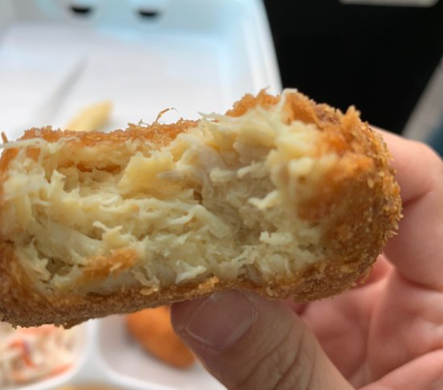 Close-up of a hand holding a crispy, golden-brown croquette, revealing a fluffy, shredded filling inside.