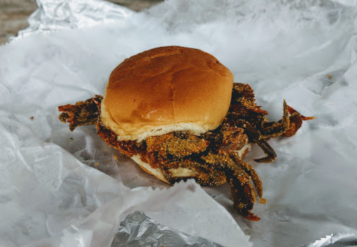 A fried soft-shell crab sandwich on a bun, served on crumpled white paper.