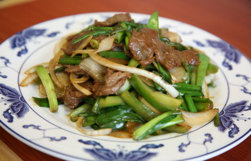 A plate of stir-fried beef with green onions and vegetables, served on a decorative blue and white dish.