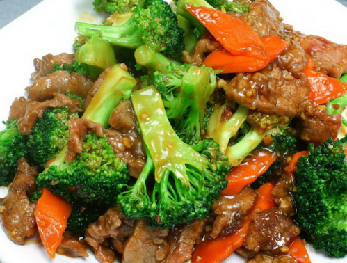 Stir-fried beef with broccoli and red bell peppers on a white plate.
