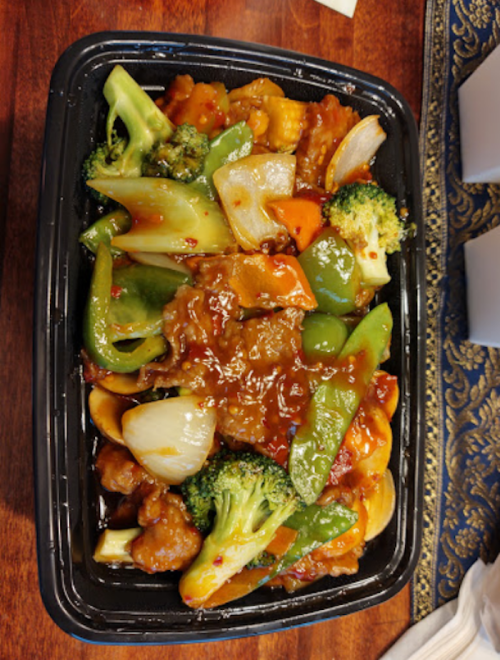 A takeout container filled with colorful stir-fried vegetables and chicken in a savory sauce.