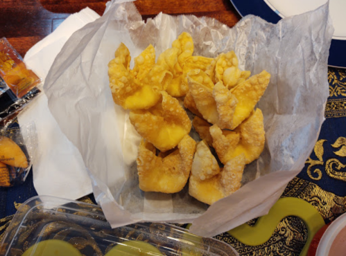 A container of crispy fried wontons arranged on a table, with fortune cookies and other food items nearby.