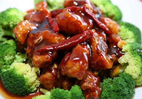 A close-up of crispy chicken in a spicy sauce, garnished with dried red chilies, served on a bed of broccoli.