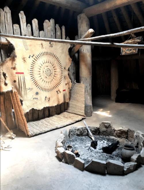 Interior of a traditional dwelling featuring a decorative wall hanging and a stone fire pit. Natural materials used throughout.