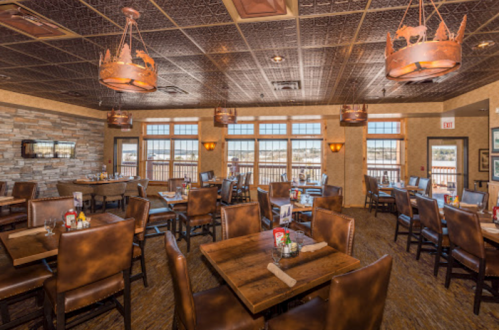 Cozy restaurant interior with wooden tables, leather chairs, and large windows, featuring rustic decor and warm lighting.