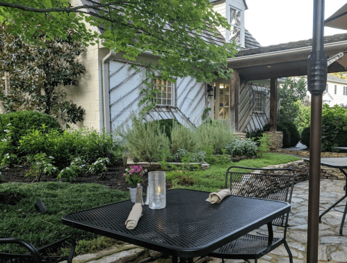 A cozy outdoor dining area with a black table, napkins, a candle, and lush greenery in the background.