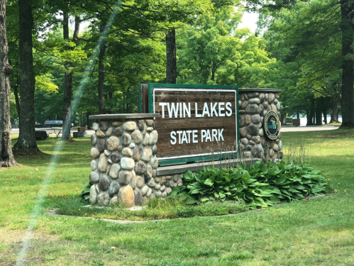 Sign for Twin Lakes State Park, featuring stone base and surrounded by green trees and grass.