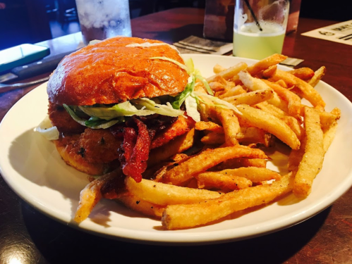 A plate with a burger topped with lettuce and bacon, served with a side of golden French fries.