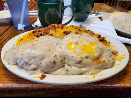 A plate of biscuits smothered in creamy gravy, topped with melted cheese and served with a side of crispy bacon.