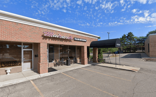 Exterior of Mainardi's Italian Restaurant, featuring a brick facade and a black awning, under a blue sky.