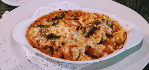 Baked pasta dish with cheese, spinach, and sauce, served in a white dish on a decorative lace doily.