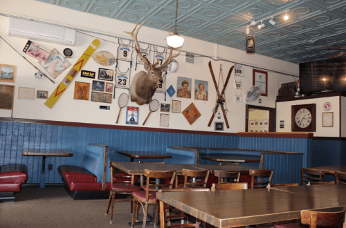 A cozy restaurant interior featuring wooden tables, red booths, and a wall adorned with vintage decor and a mounted deer head.