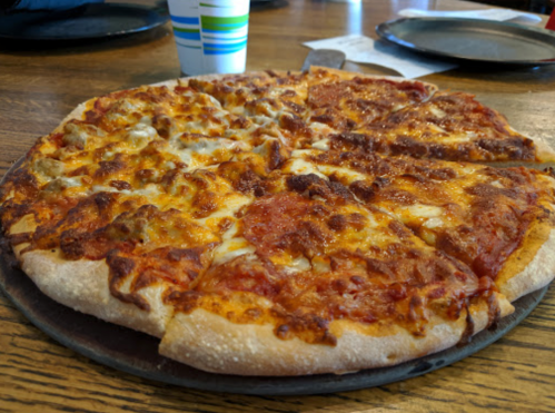 A freshly baked pizza with a golden crust, topped with cheese and various meats, served on a wooden table.