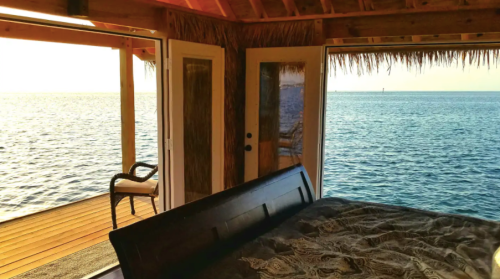 Cozy interior of a beachfront bungalow with a view of the ocean through open doors and a sunlit deck.