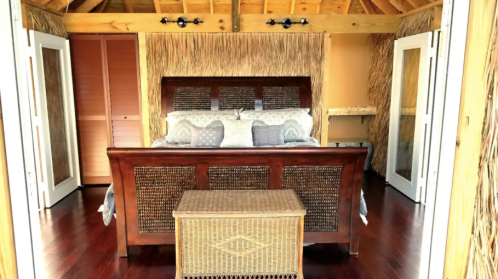 Cozy bedroom with a wooden bed, decorative pillows, and a woven storage chest, featuring a warm, natural aesthetic.