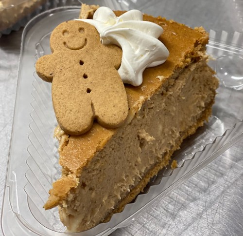 A slice of gingerbread cheesecake topped with whipped cream and a gingerbread cookie.