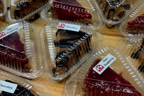 Slices of chocolate and raspberry cheesecake in clear plastic containers, arranged on a wooden surface.