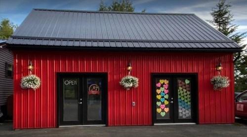 A red building with a metal roof, featuring two doors adorned with colorful heart decorations and an "OPEN" sign.