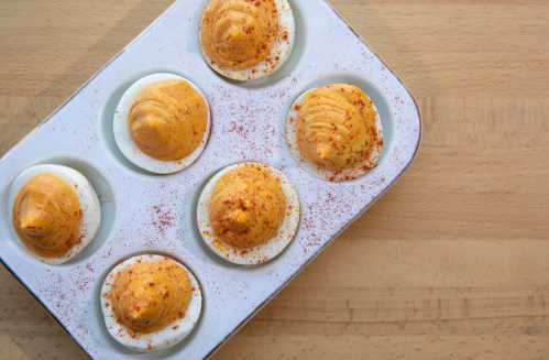 A tray of deviled eggs topped with paprika, featuring creamy orange filling and white egg whites.