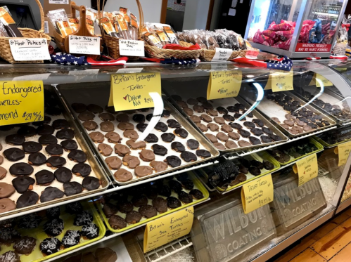 A display case filled with various chocolate treats, including cookies and turtles, labeled with prices.