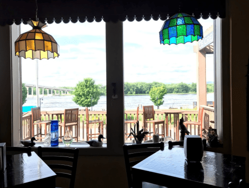 View from a restaurant window showing a river, outdoor seating, and colorful stained glass lamps.