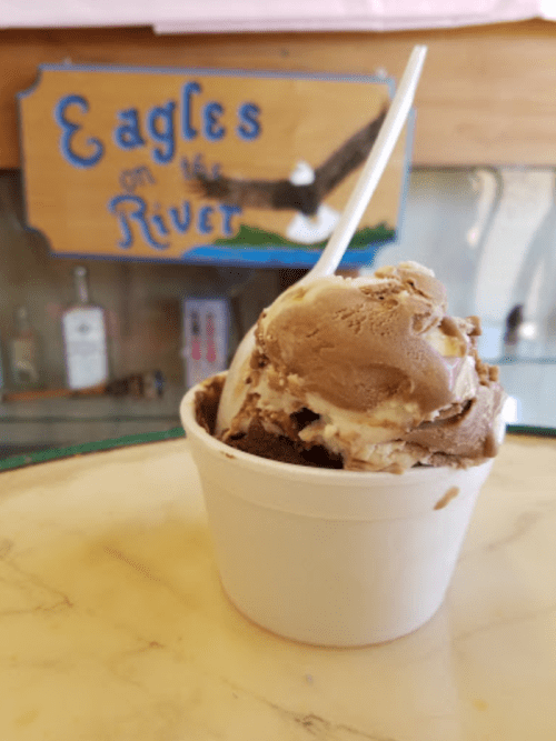 A cup of chocolate ice cream with swirls, placed on a marble surface near a sign that reads "Eagles on the River."