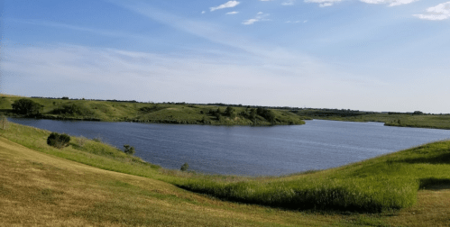 A serene landscape featuring a calm lake surrounded by green hills under a clear blue sky.