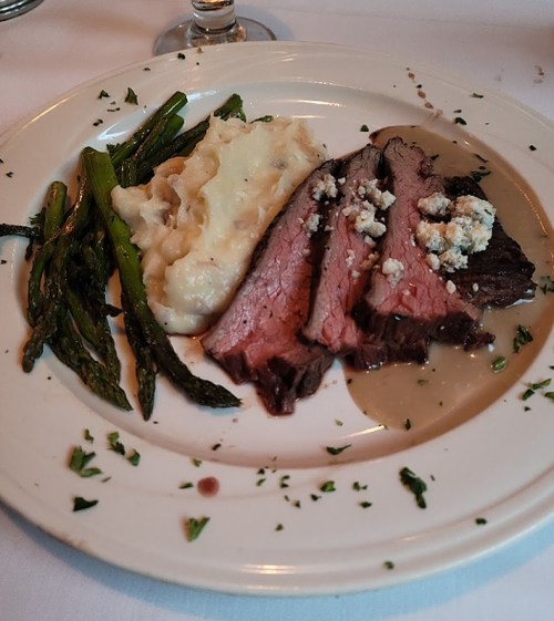 A plate featuring sliced beef, creamy mashed potatoes, and asparagus, garnished with herbs.