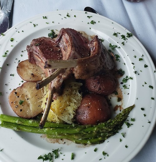 A plate of lamb chops with roasted potatoes, asparagus, and a bed of sauerkraut, garnished with herbs.