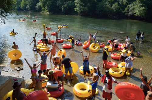 A lively river scene with people in colorful inner tubes, enjoying a sunny day and splashing in the water.