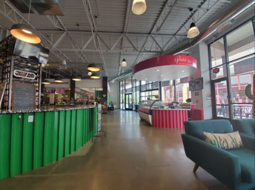 A spacious, modern café interior with colorful decor, a gelato counter, and seating areas. Bright and inviting atmosphere.