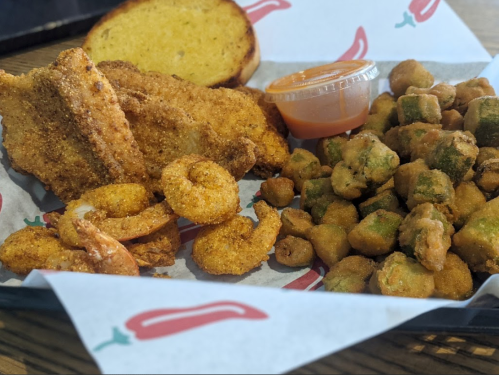 A plate of fried shrimp, fish fillets, and fried okra with a side of dipping sauce and a slice of toasted bread.