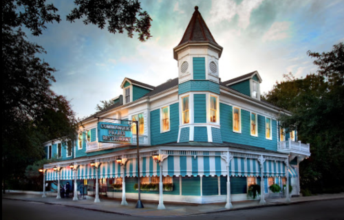 A charming blue and white restaurant with a tower, featuring large windows and striped awnings, set against a cloudy sky.
