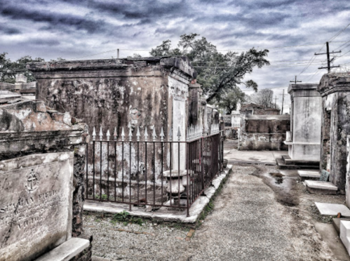 A desolate cemetery with weathered tombs, iron fences, and a cloudy sky, creating a somber atmosphere.