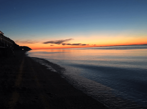 A serene beach at sunset, with calm waters reflecting vibrant orange and blue hues in the sky.
