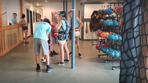A group of people in a facility preparing for an outdoor activity, with climbing gear and helmets displayed nearby.