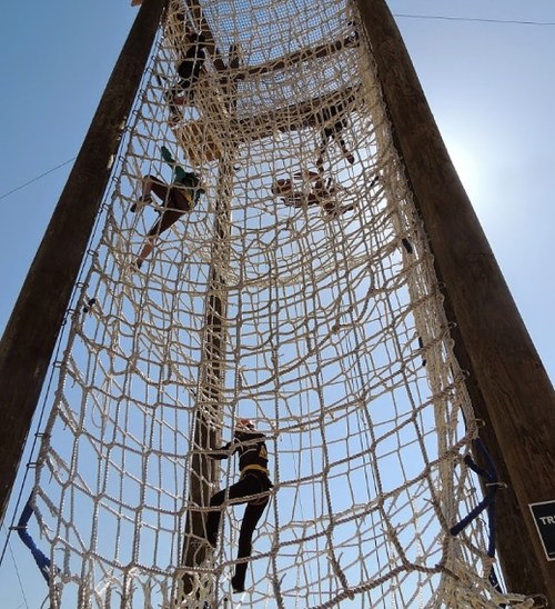 People climbing a large rope net structure against a clear blue sky.