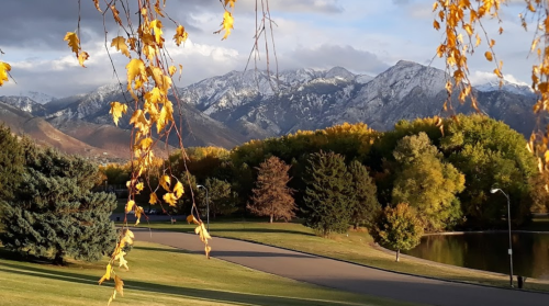 Scenic view of mountains with snow, colorful autumn leaves, and a peaceful park with a winding path and pond.