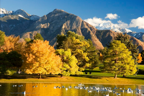 A serene lake surrounded by colorful autumn trees and majestic mountains under a clear blue sky.