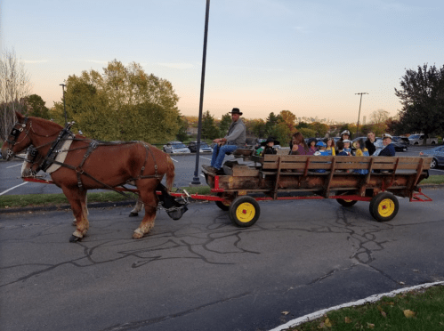 A horse-drawn wagon carries a group of children, with a man guiding the horse, set against a sunset backdrop.
