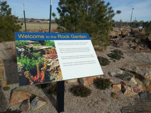 Sign reading "Welcome to the Rock Garden" with information about the garden's plants and features, surrounded by rocks and greenery.