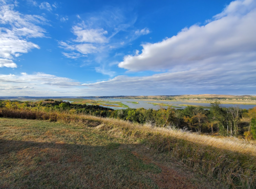 A scenic view of a river winding through green fields under a blue sky with scattered clouds.
