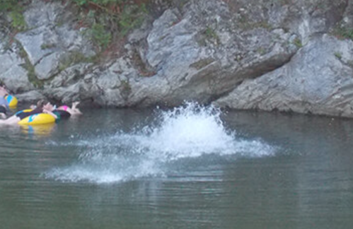 A splash of water in a serene natural setting, with rocky edges and colorful inflatable tubes nearby.
